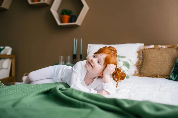 Linda chica pelirroja feliz niño acostado en la cama en casa — Foto de Stock