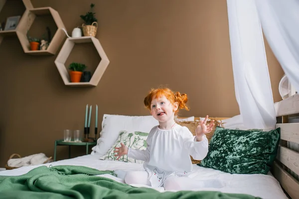 Bonito feliz pouco ruiva menina sentado no cama dentro de casa — Fotografia de Stock