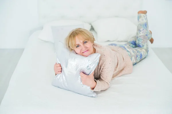 Mujer mayor sonriente descansando en el dormitorio, abrazando la almohada —  Fotos de Stock
