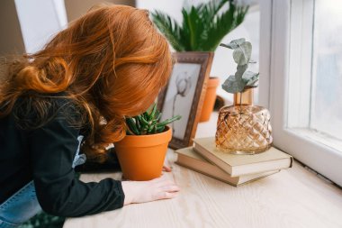 Güzel Redhead litlle kız masa içinde pot yeşil çiçek, kitap oturan