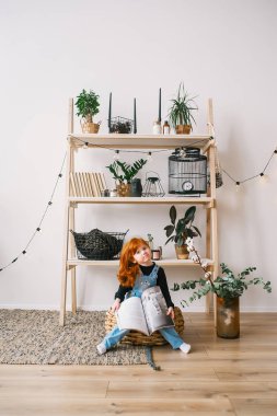 Güzel Redhead litlle kız şık dergi ile büyük bir sepet üzerinde oturuyor 