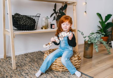 Güzel Redhead litlle kız elinde çiçek şube ile bir sepet üzerinde oturuyor