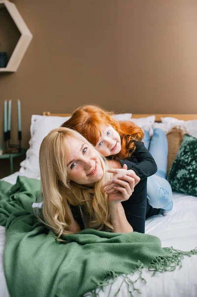 Retrato de jovem mãe e pequena filha ruiva deitada na cama . — Fotografia de Stock