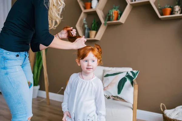 Чарівна руда дівчинка виглядає осторонь, поки її мати розчісує волосся дочки — стокове фото