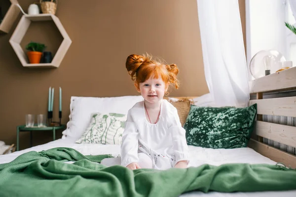 Bonito feliz ruiva menina criança sentada na cama em casa — Fotografia de Stock