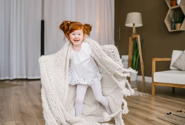 Little redhead girl with plaid dances at home