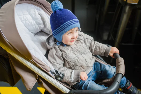 Carino bambino in abiti caldi si siede in un passeggino al chiuso — Foto Stock