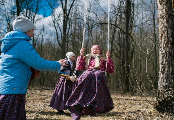 O festival pagão da primavera. Crianças balançando no balanço alto, contra o fundo de uma floresta de primavera — Fotografia de Stock