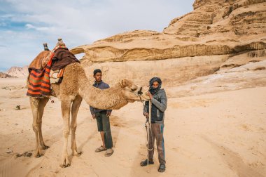 Wadi Rum kaya arka planda deve duran iki Bedevi adamla çöl. Ürdün.