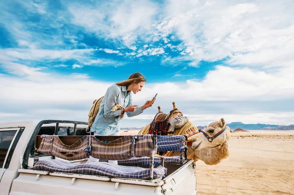 Uśmiechnięta młoda kobieta w samochodzie robi zdjęcie wielbłąda w środku pustyni Wadi Rum w Jordanii. — Zdjęcie stockowe
