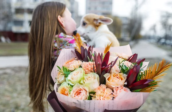 Hermosa mujer con un ramo de flores sostiene un cachorro en sus manos. Enfoque selectivo en flores — Foto de Stock