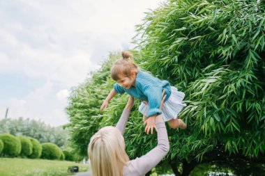 Anne ellerini tutar, parkta yaz aylarında kızı ellerini asansörler kusuyor. Doğada anne ve çocuk.