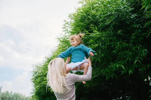 Glückliche junge Familie an einem Sommertag im Stadtpark. werfen das kleine Mädchen in die Luft. — Stockfoto