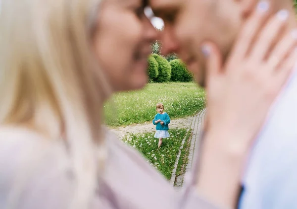 Closeup of happy couple with her little daughter kissing over a park background. Focus on children. — Stock Photo, Image