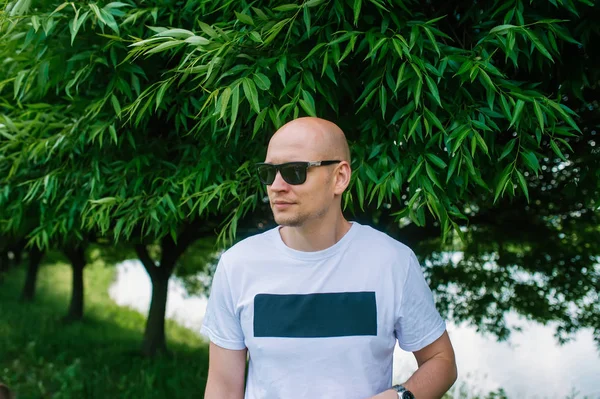 Kale knappe man in zonnebril op witte tshirt is in zomerpark. — Stockfoto