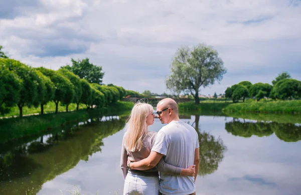 Visão traseira do adorável casal homem e mulher sentado perto do rio ou lago abraçando e relaxando . — Fotografia de Stock