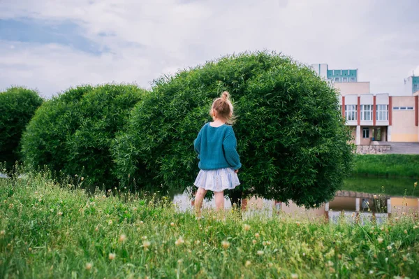 Mała dziewczynka chodzić w trawie na Pak miasta w pobliżu stawu. Widok z tyłu — Zdjęcie stockowe