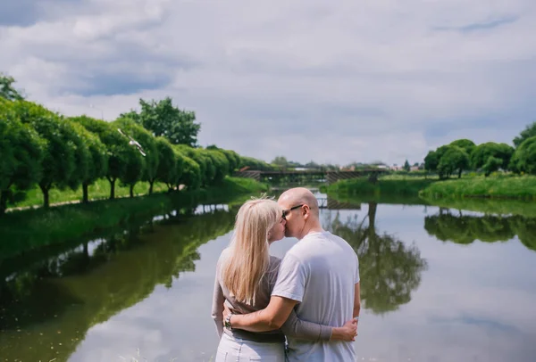 Feliz joven pareja de pie y besándose en verano cerca del lago —  Fotos de Stock