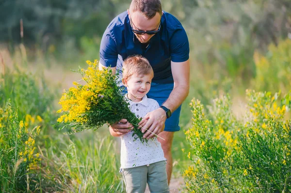 Sonriente niño y su padre disfrutando al aire libre en el campo de flores silvestres —  Fotos de Stock