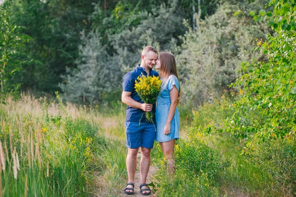 Casal apaixonado na natureza com um buquê de flores amarelas selvagens . — Fotografia de Stock