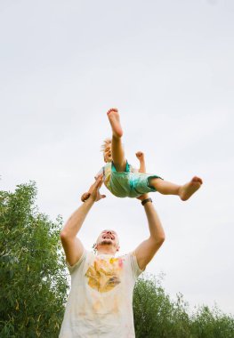 Baba ve küçük oğlu açık havada oynuyor, çocuk havada uçuyor.