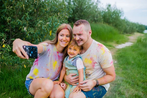 Smiling family in multi-colored paints taking selfie on summer meadow. Family portrait — Stock Photo, Image