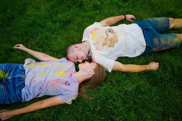 Det romantiska paret med mångfärgade puder på sina kroppens på gräset i parken. Uppifrån och. — Stockfoto