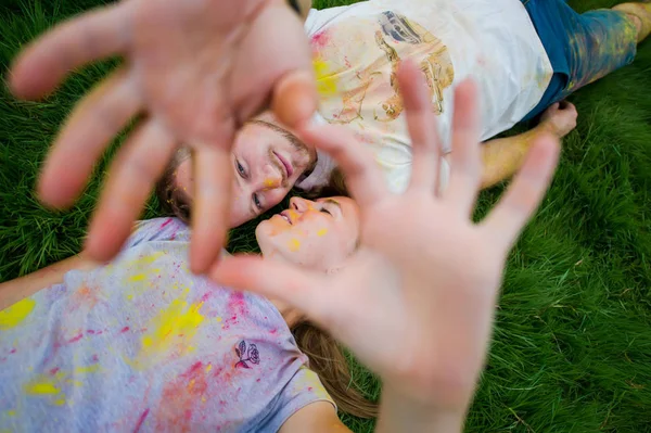 Pareja feliz con camisas sucias tumbadas sobre hierba verde en el parque y haciendo corazones con sus manos. Vista superior — Foto de Stock