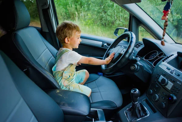 Divertente ragazzo con il viso sporco macchiato con vernice che tiene le mani sul volante in auto . — Foto Stock