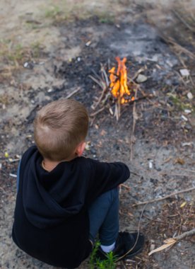 Küçük çocuk piknikte ateşin yanında otur. Seyahat, yürüyüş, durma konsepti. Üstte görüntü