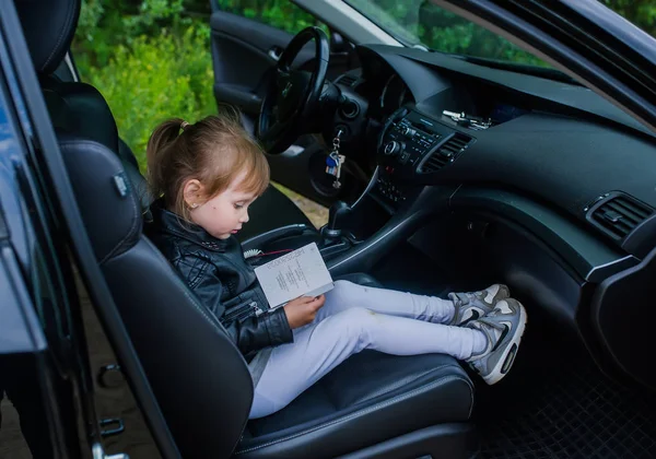 Carina bambina con passaporto sedersi in un seggiolino auto pronto per un giro con i genitori . — Foto Stock