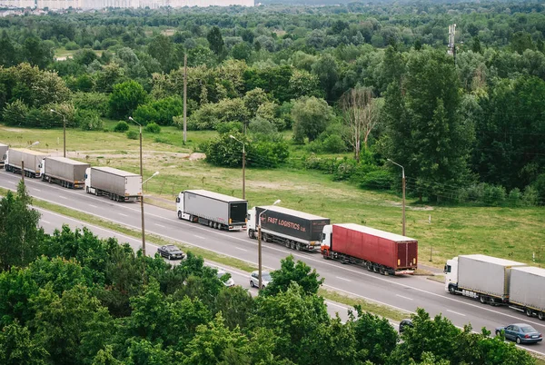 A nemzetközi határon áthaladó teherautók sora, piros és különböző színű teherautók dugóban az úton. — Stock Fotó