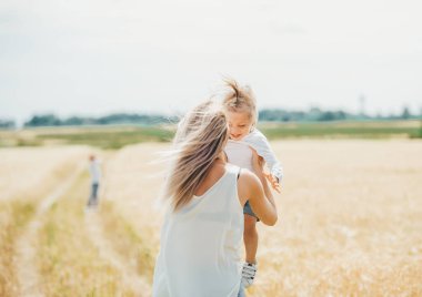 Anne buğday alanında küçük bir gülümseyen kız tutan. 