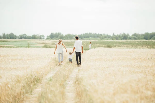 Szczęśliwa rodzina chodzenie na ścieżce w polu pszenicy w czasie dnia. Koncepcja przyjaznej rodziny. — Zdjęcie stockowe