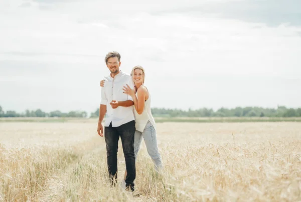 Joven feliz pareja bastante soleada está de pie de moda y sonriendo en las espiguillas en el fondo del campo —  Fotos de Stock