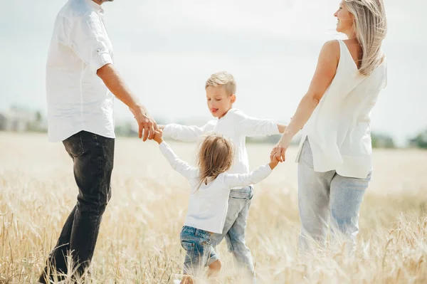 Happy family of four holding hands dancing in circle on a wheat field. — Stock Photo, Image