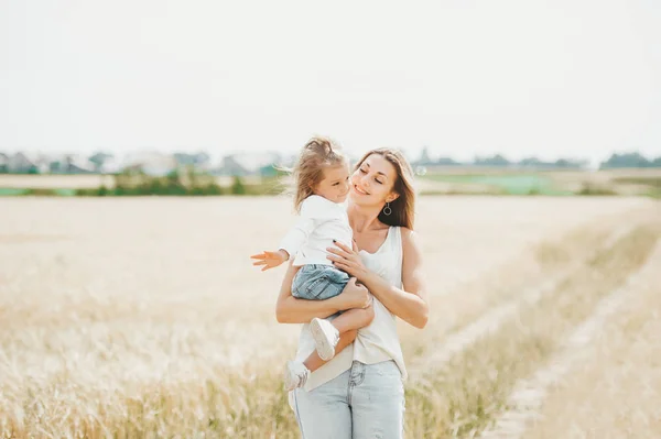 Mamma som håller en liten leende flicka på vete fältet. — Stockfoto