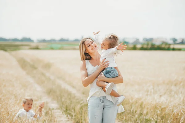 Мама держит маленькую улыбающуюся девочку на пшеничном поле. Мать с детьми на открытом воздухе — стоковое фото