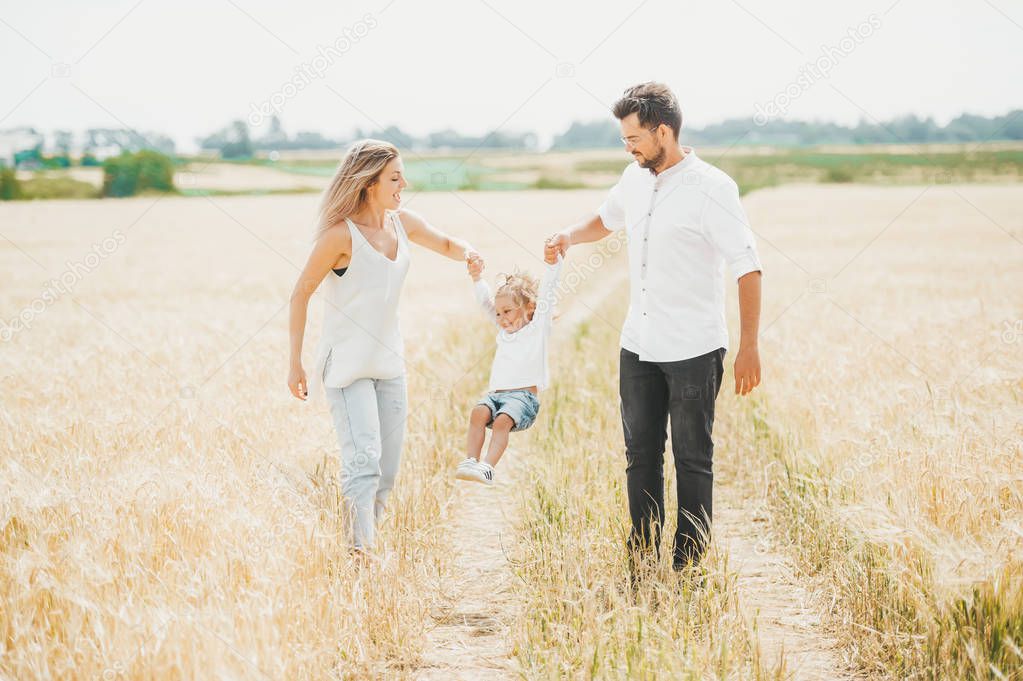 Cute little girl on walk with parent in wheat field on sunny day. Family vacation concept with copy space