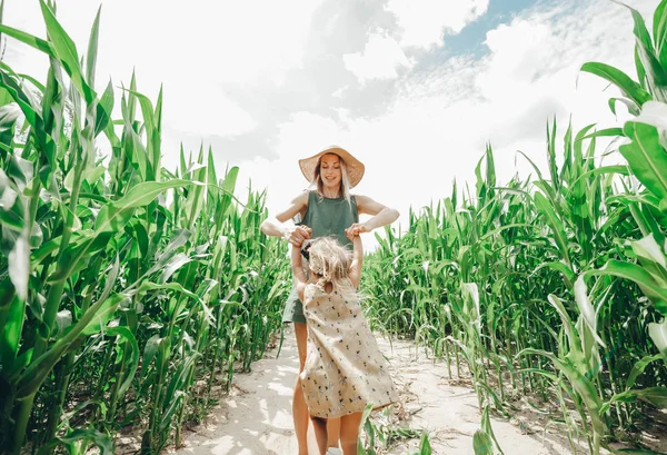 一个年轻的美丽的母亲与她的小可爱的女儿在玉米地的乐趣。国家的自然. — 图库照片