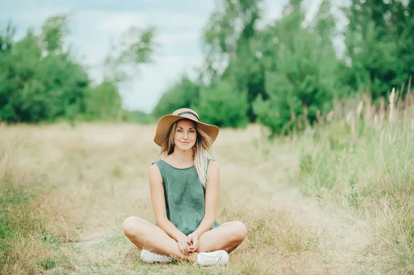 Portret uśmiechniętej dziewczyny w kapeluszu siedzi w lotosu stwarzają na zewnątrz. — Zdjęcie stockowe