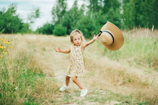 Маленькая счастливая веселая девочка играет и веселится с большой шляпой на природе — стоковое фото
