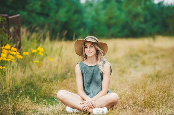 Uśmiechnięta młoda kobieta w kapeluszu siedzieć w Lotos stwarzają na lato łąka. — Zdjęcie stockowe