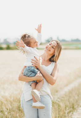 Anne buğday alanında küçük bir gülümseyen kız tutan.