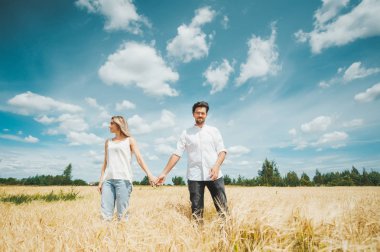 Mavi gökyüzü arka plana karşı sahada yürürken genç çift el tutarak