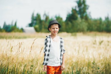 Avrupa okul çağındaki çocuk, köydeki bir buğday tarlasının arka planına karşı siyah şapkalı