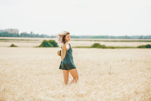 Mujer feliz con sombrero de paja en las manos disfrutando del sol en el campo de cereales . — Foto de Stock