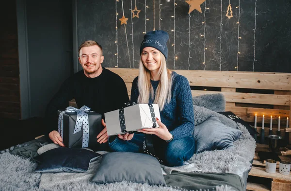 Retrato de mulher feliz em boné azul e homem com caixa de presente na cama descansando juntos em casa . — Fotografia de Stock