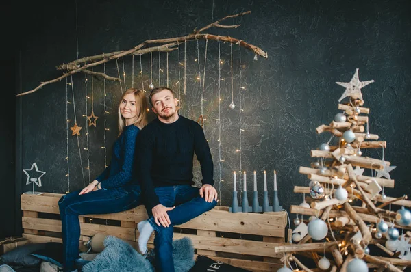 Pareja joven cerca de abeto de Navidad en la habitación con la pared decorada para Navidad . —  Fotos de Stock