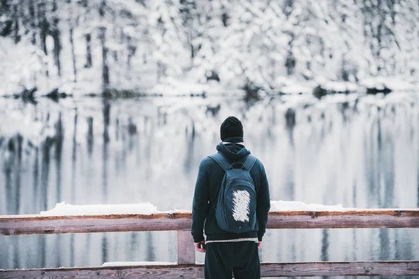 Ein junger Mann mit Rucksack bewundert die malerische Landschaft des Wintersees. — Stockfoto